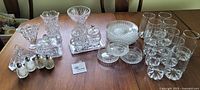 Full lot displayed on dining table showing a variety of clear crystal glassware and tableware including plates, glasses, vases, and salt and pepper shakers.
