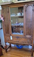 Front view of wooden dining cabinet showing glass center door and side wood panels with decorations, drawer below.