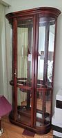 Full view of the glass and wood curio cabinet showing the tall, narrow design with curved glass panels and glass shelves inside.