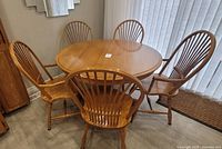 Wide shot of round wooden kitchen table surrounded by six matching spindle-back chairs with armrests.