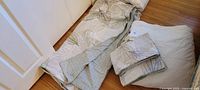Photo showing the folded duvet cover and duvet on the floor, displaying the sage green leaf print and beige background.