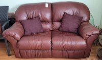 Front view of burgundy pleather loveseat couch with two pillows.