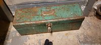 Photo of rusty green metal tool box closed on concrete floor.