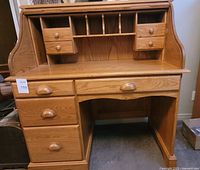Full front view of oak roll-top desk with open top, showing drawers and cubby holes.