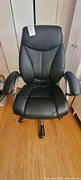 Front view of black office chair showing padded seat and backrest, and cushioned armrests with some wear