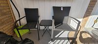 Two black outdoor rattan chairs with a small black square table between them on a porch