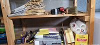 Shelf with multiple pairs of work gloves, paint scrapers, brushes, sanding paper, and rolls of tape and disposable gloves.