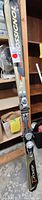 Full length view of one Rossignol ski showing bindings and overall condition, with shelving and items in the background.