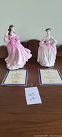 Two Royal Doulton figurines Lauren and Eleanor with their Certificates of Authenticity placed on a wooden surface.