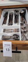 Image of stainless steel cutlery set organized in a drawer tray including forks, knives, tablespoons, teaspoons, and large soup spoons.