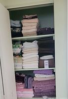 Three shelves filled with various folded towels in multiple neutral and pastel colors inside a closet.
