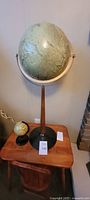 Vintage globe on mid-century modern style stand shown on a wooden table from angled side view.