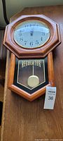 Full view of the dark maple wood framed wall clock showing octagonal top, clock face with black Arabic numerals on white, and pendulum with REGULATOR label below.