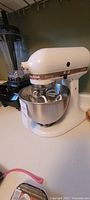 White KitchenAid Ultra Power MixMaster stand mixer on countertop with stainless steel bowl and mixer attachments inside bowl.