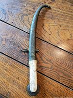 Full side view of curved dagger in scabbard on wood surface