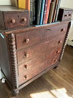 Front angle of antique mahogany dresser showing four drawers with wooden knobs, hand carved spiral supports on sides, and visible scratches and chipping.