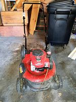 Front angle showing Craftsman red lawn mower with Briggs & Stratton Gold engine, black handlebar, and four wheels on concrete garage floor.