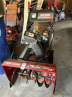 Front angled view of Craftsman Snow King snow blower showing red steel auger housing with 9.0 HP 28-inch clearance, rubber tracks and control panel with labels.