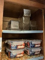 Glass butter dish and Luminarc glass Tupperware containers stacked in wooden cabinet shelf.