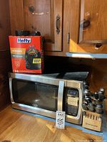 Oster microwave, Hefty trash bags box, Wusthof knife block with knives on wooden counter next to wood-paneled wall.