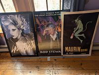 Three music posters framed resting on the floor: Lady Gaga, Rod Stewart, and Maurin Quina.