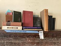 Wide view of collection showing all books, rosary beads, and vintage stamp book on wooden shelf