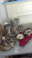 Wide shot of the collection showing silver plated trays, pewter ice buckets, teapot, flatware, and utensils arranged on a table.