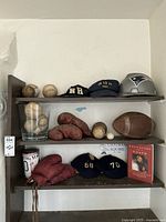 Photo of sports items including vintage baseballs, baseball caps, boxing gloves, football, and the book 'The Education of a Coach' on shelves.