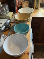 Stack of six mixing bowls of varying sizes and colors including white, beige, and blue ceramic bowls on wooden countertop.