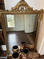 Photo showing the brass mirror with intricate design, the bronze boot, and the brass vase positioned in front.