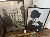 Two framed black and white prints leaning on a wall: Paris cityscape and Charlie Chaplin portrait.