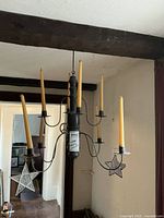 Front view of rustic black metal hanging candelabra with six yellow candles and star ornaments