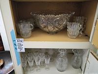 Two-shelf view showing top shelf punch bowl with cups and bottom shelf decanter, glasses, and pitcher