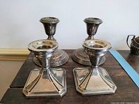Front view of two pairs of sterling silver candle holders showing square base set in front and rounded base set behind, exhibiting tarnish.