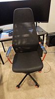 Front view of IKEA HUVUDSPELARE black gaming chair with mesh back and red accent armrests.