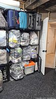 Photo of black metal shelving unit fully assembled in a basement storage room, containing bags and luggage but contents not included in sale.