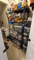 Full view of the black metal shelving unit in a toy closet, shelves holding various toys and plastic bins, metal frame and wire shelves visible.