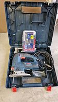 Opened carrying case showing Bosch JS572E jigsaw tool, power cord, and 30-piece blade set