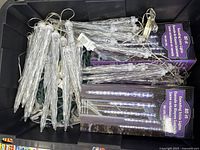 Multiple cascading icicle string light sets in black storage bin with two unopened boxed sets visible.