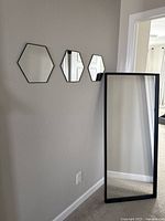Floor length mirror leaning against wall with three small decorative hexagonal mirrors mounted horizontally on wall beside it.
