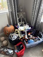 Photo of large plastic skeleton sitting with Halloween decorated bins and pumpkin nearby, showing lot contents