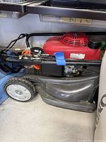 Side view of red Honda engine housing attached to black mower deck and wheels