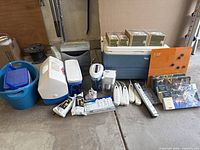 View showing multiple coolers (Igloo MaxCold, Playmate, Coleman), water pitchers with filtering systems (ZeroWater, Brita), Aurora paper shredder, several Belkin surge master extension cords, orange magnetic message board, and a few boxed items including hanging glass vases.