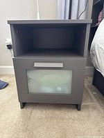 Front view of charcoal gray matte laminate nightstand showing open shelf and frosted glass drawer with handle.