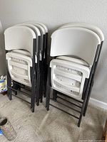Stacked set of 7 folded white plastic folding chairs with gray metal frames.