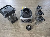 Ninja Ultima blender base, large pitcher, three single-serve cups, and blade assembly on wooden surface.