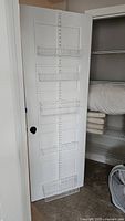 Photo of a white over the door metal wire hanging storage rack mounted on a white door with four baskets arranged vertically.
