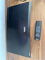 Top view of Samsung K8500 Blu-ray Player with remote control on wooden surface.