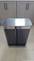 Front view of the Simple Human dual trash and recycling unit showing two black compartments with stainless steel top and foot pedal base.