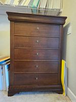 Front view of the dark wood tall dresser showing five drawers with brass hardware.